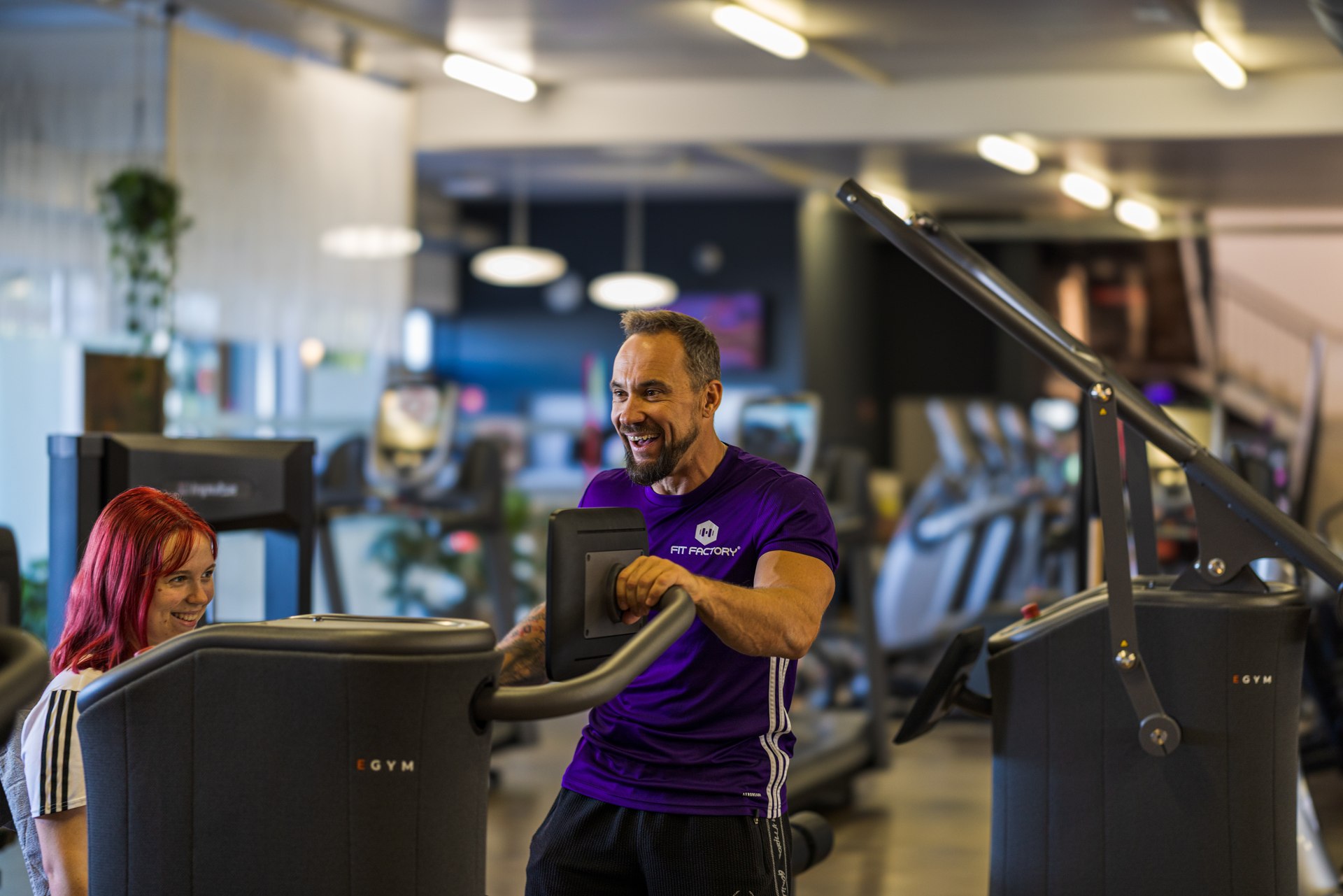 Marc im violetten FITfactory-Shirt begleitet eine Trainierende am EGYM-Gerät.