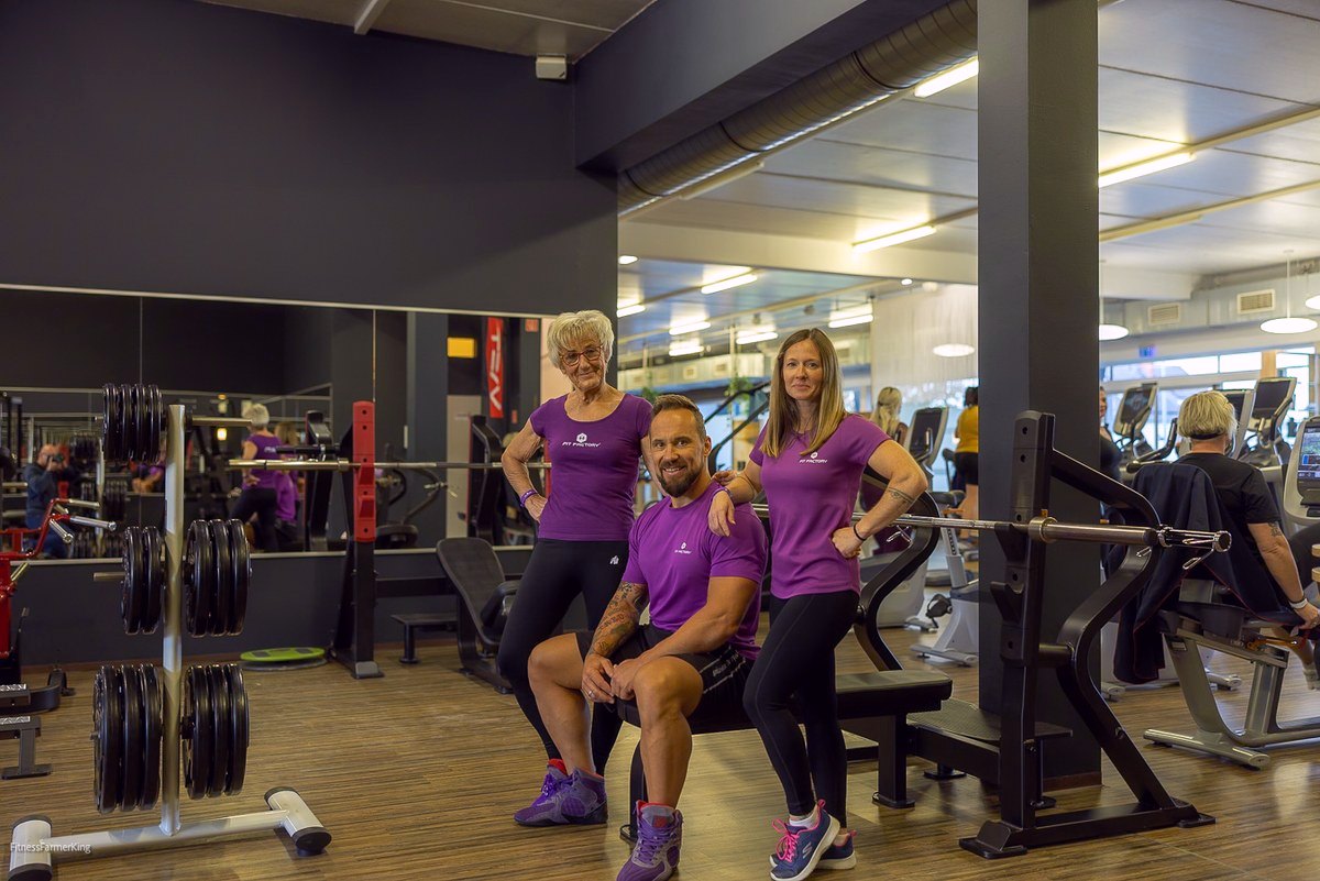 Drei Erwachsene in FITfactory-Kleidung in einem Trainingsbereich.
