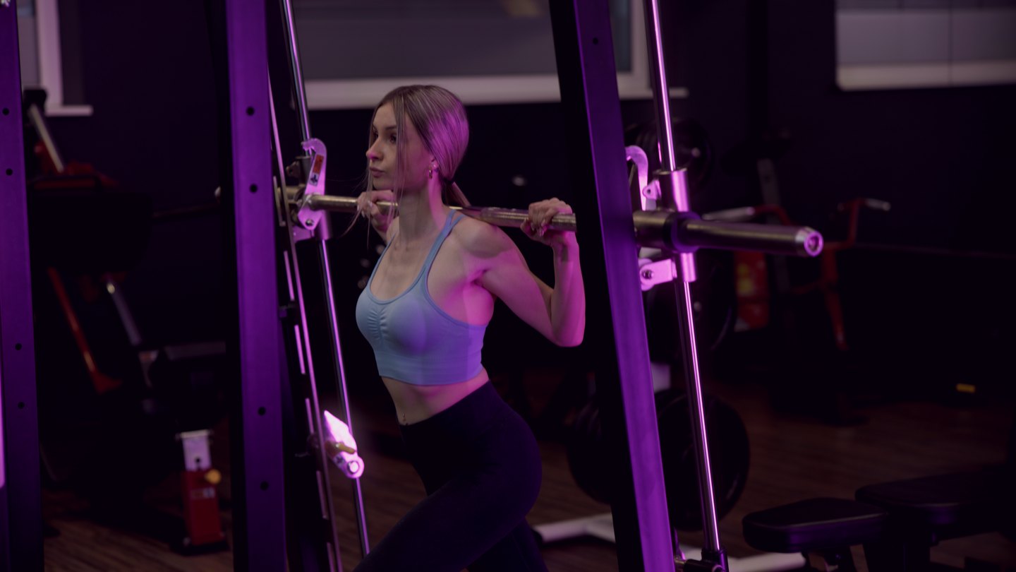 Eine junge Frau trainiert konzentriert mit einer Langhantel in einem FITfactory Studio